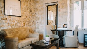 Una sala de estar con pared de piedra, un sofá, una mesa de centro, una silla y una mesa de comedor con un hervidor.