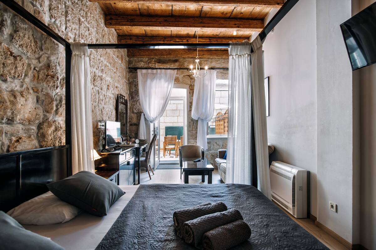Een slaapkamer met een groot bed, een bureau en een stoel, met stenen muren en houten balken.