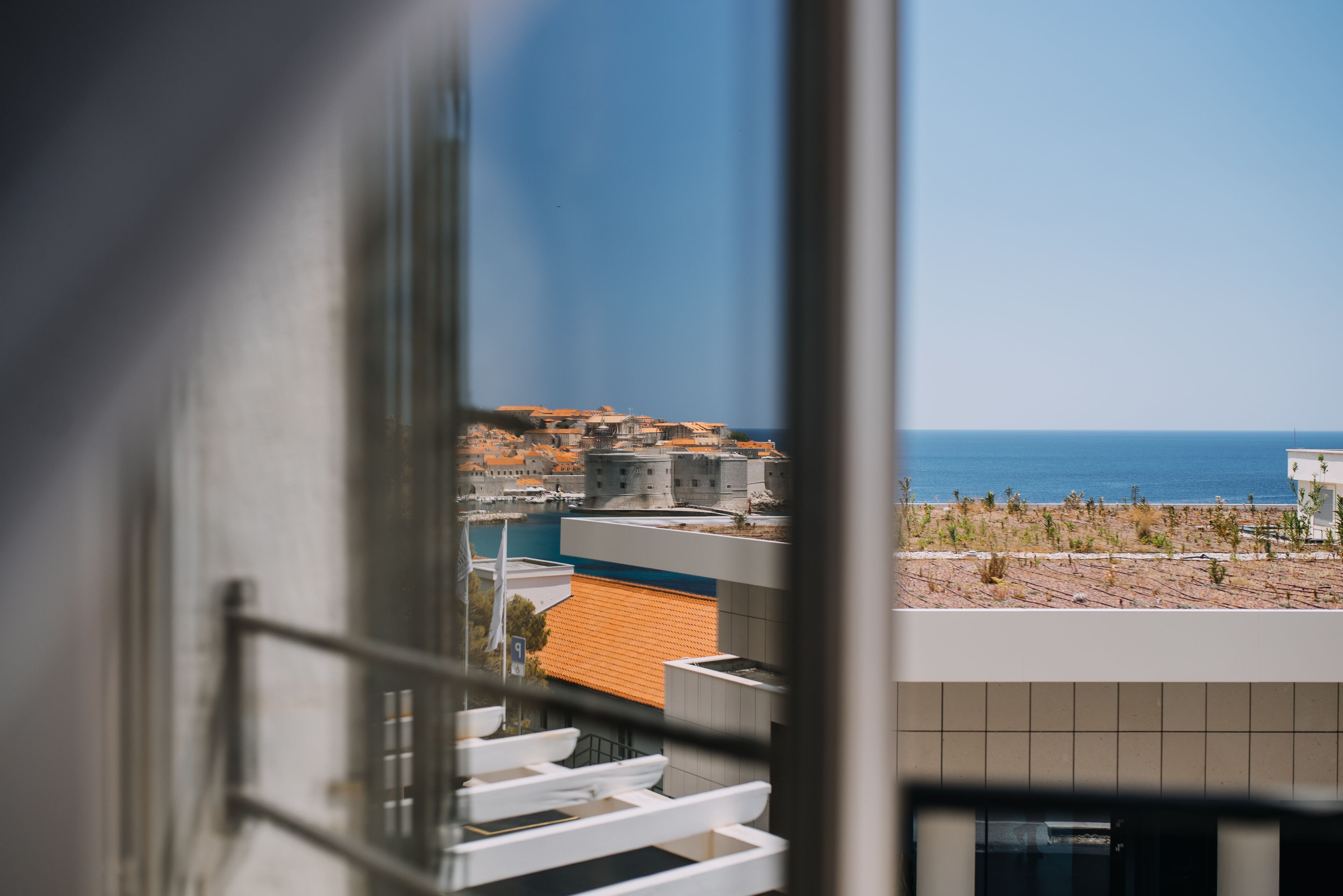 A view from a window overlooking a coastal town with buildings and a clear blue sky.