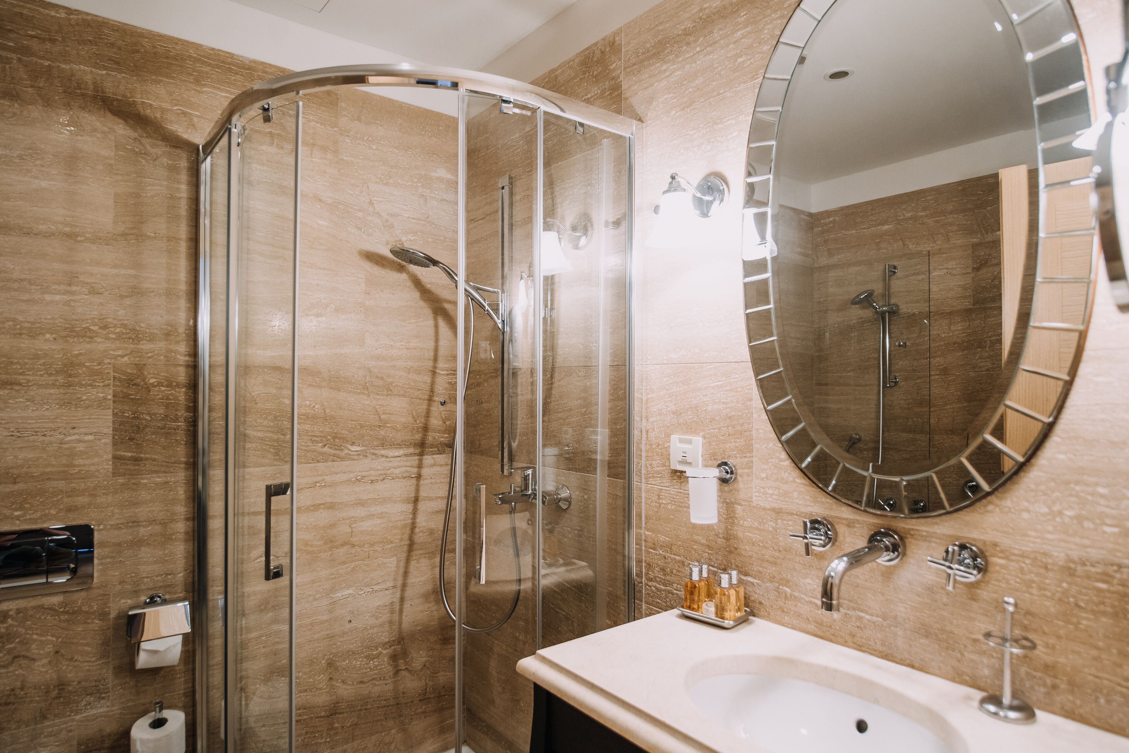 A modern bathroom with a glass-enclosed shower, a large mirror, and a sink with toiletries.