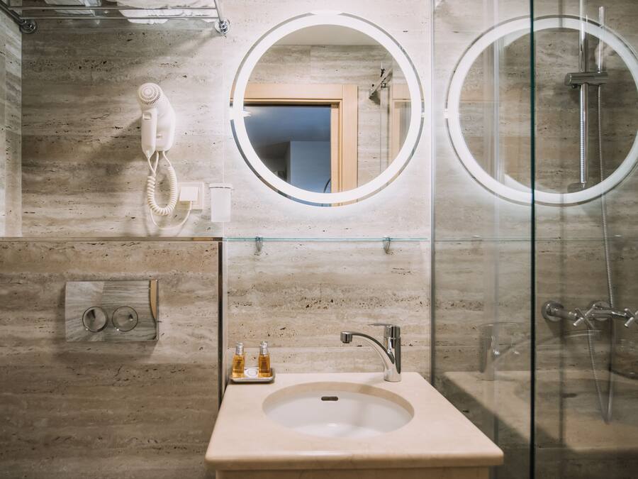 Uma casa de banho moderna com cabine de duche em vidro, lavatório com espelho acima e secador de cabelo fixado na parede.