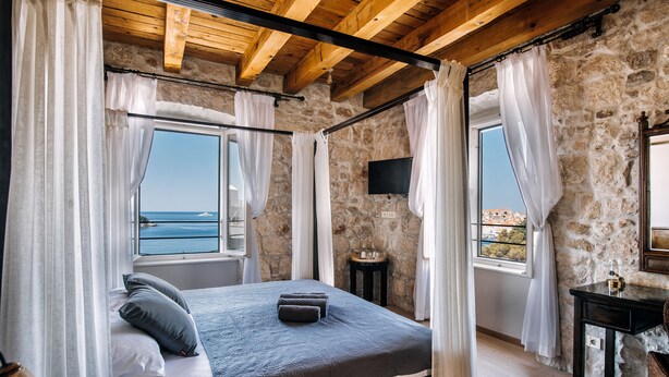 Un dormitorio con pared de piedra, una cama con ropa de cama gris, una mesita de noche y un televisor en la pared.