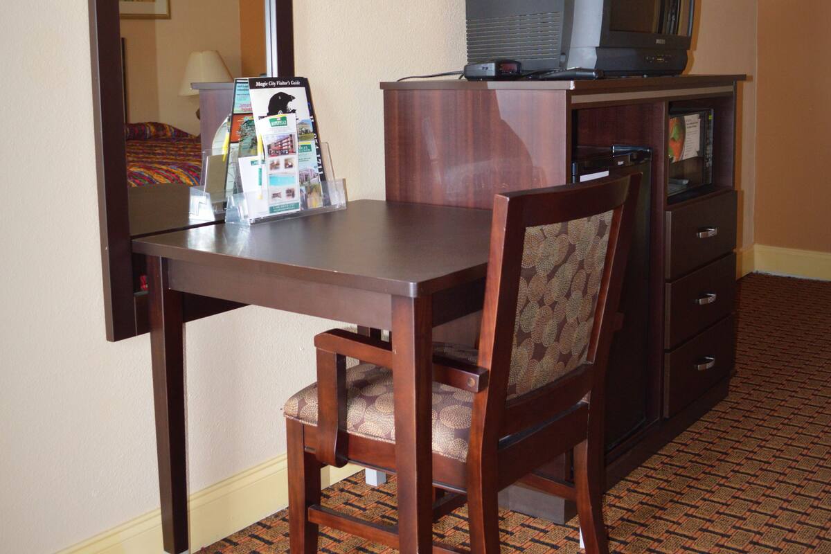 A hotel room with a wooden desk, a chair, a television on a cabinet, and a mirror on the wall.