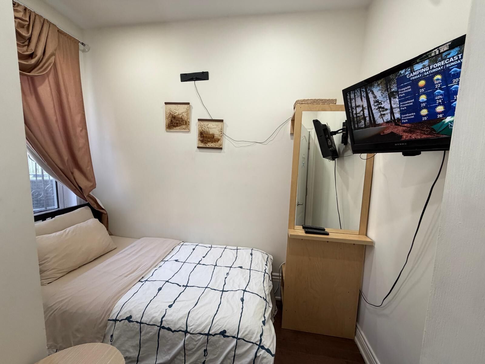 Ein Schlafzimmer mit einem Bett, einem an der Wand befestigten Fernseher und einem Fenster mit Vorhängen.