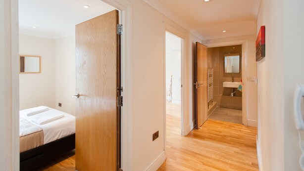 Habitación de hotel con puerta de madera, cama con ropa blanca, una mesita de noche pequeña y un buró.