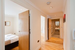 A hotel room with a wooden door, a bed with white linens, a small bedside table, and a nightstand. - London Serviced Apartments (London)