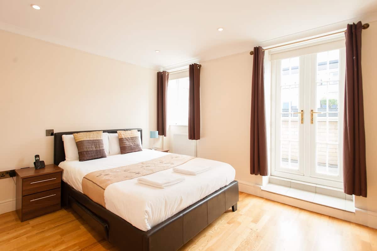 A modern bedroom with a large bed, wooden floor, and a window with curtains.