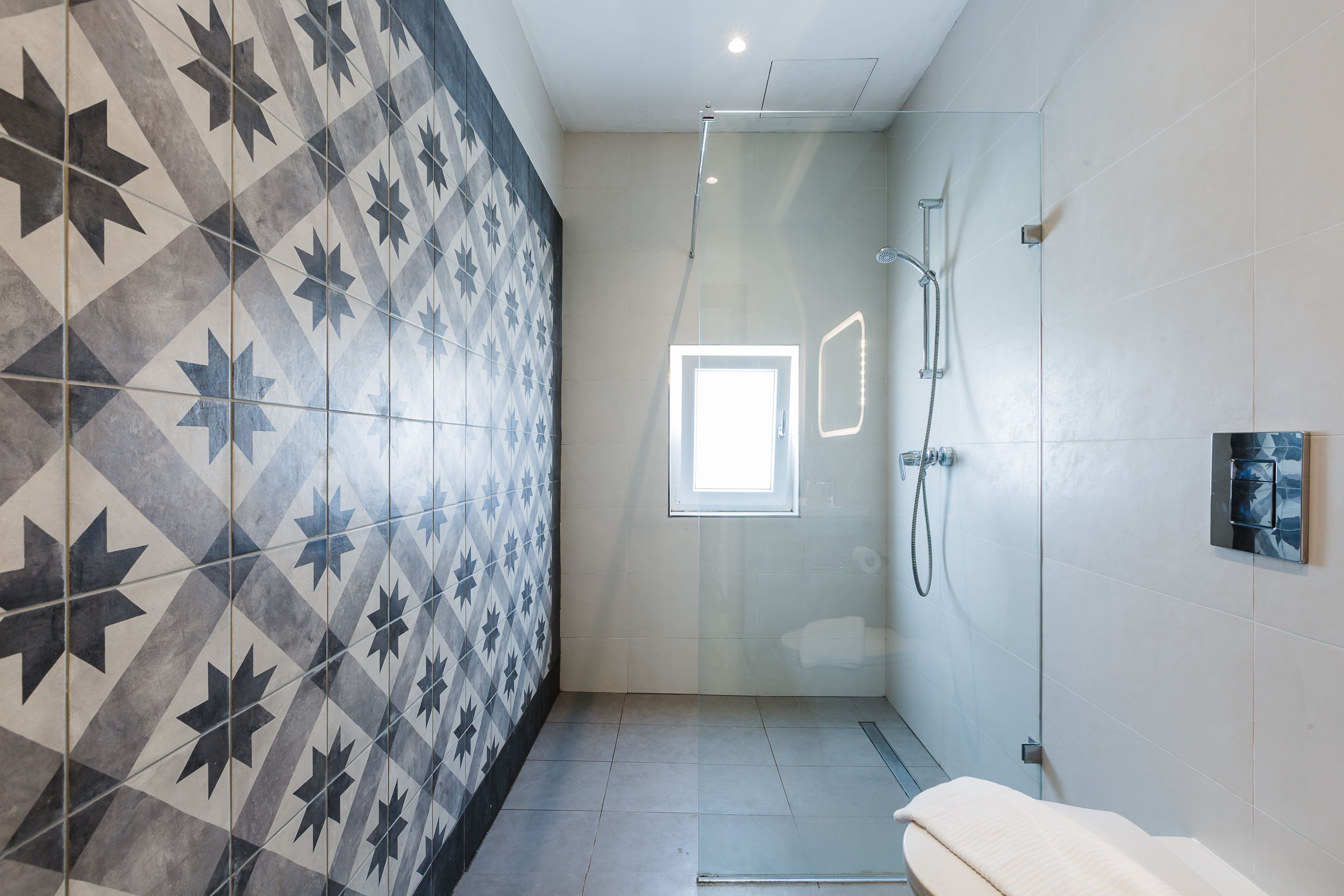 A modern bathroom with a geometric tile pattern, a glass shower enclosure, and a visible window.