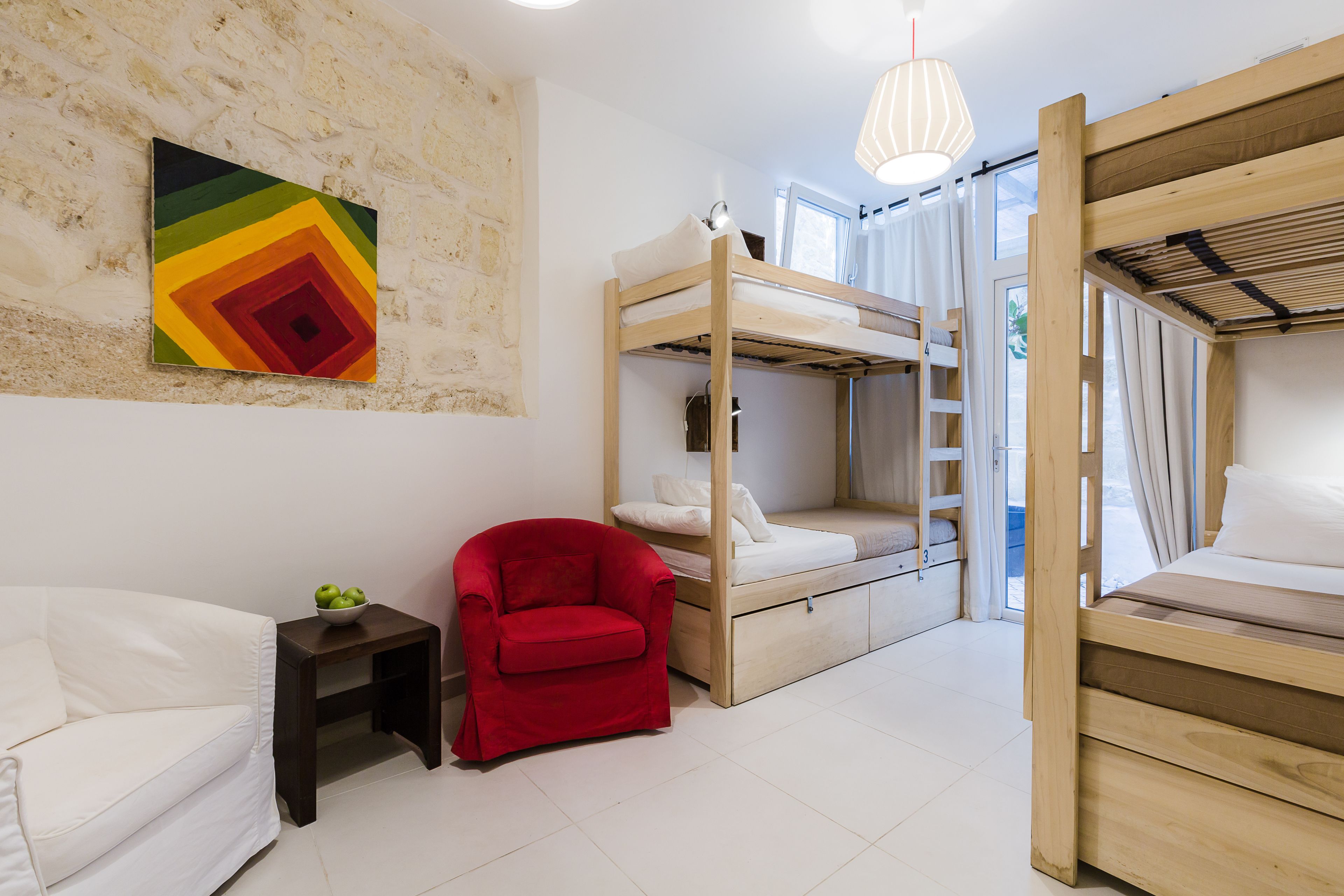 A room with bunk beds, a red chair, a small table, and a colorful wall art piece.