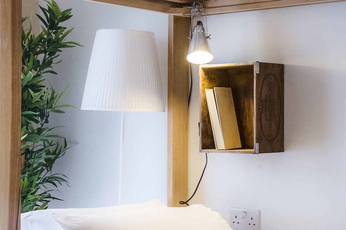 A neatly made bed with white linens, a bedside lamp, and a small wooden cabinet with books.