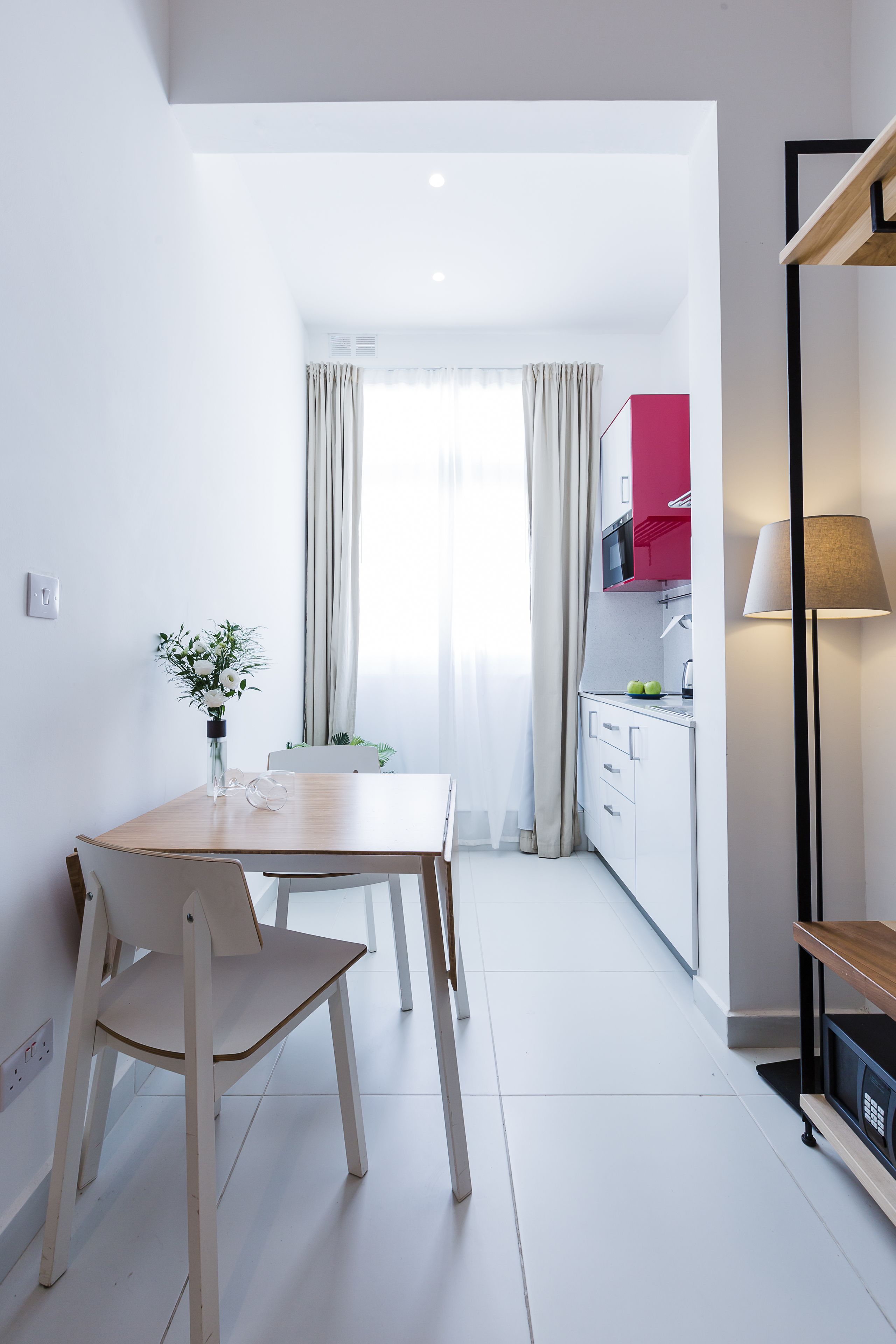 A modern kitchen with white cabinets, a red microwave, and a dining area with a wooden table and chairs.