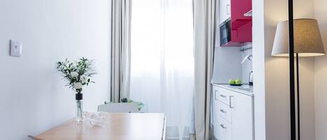 A modern kitchen with white cabinets, a red microwave, and a dining area with a wooden table and chairs.