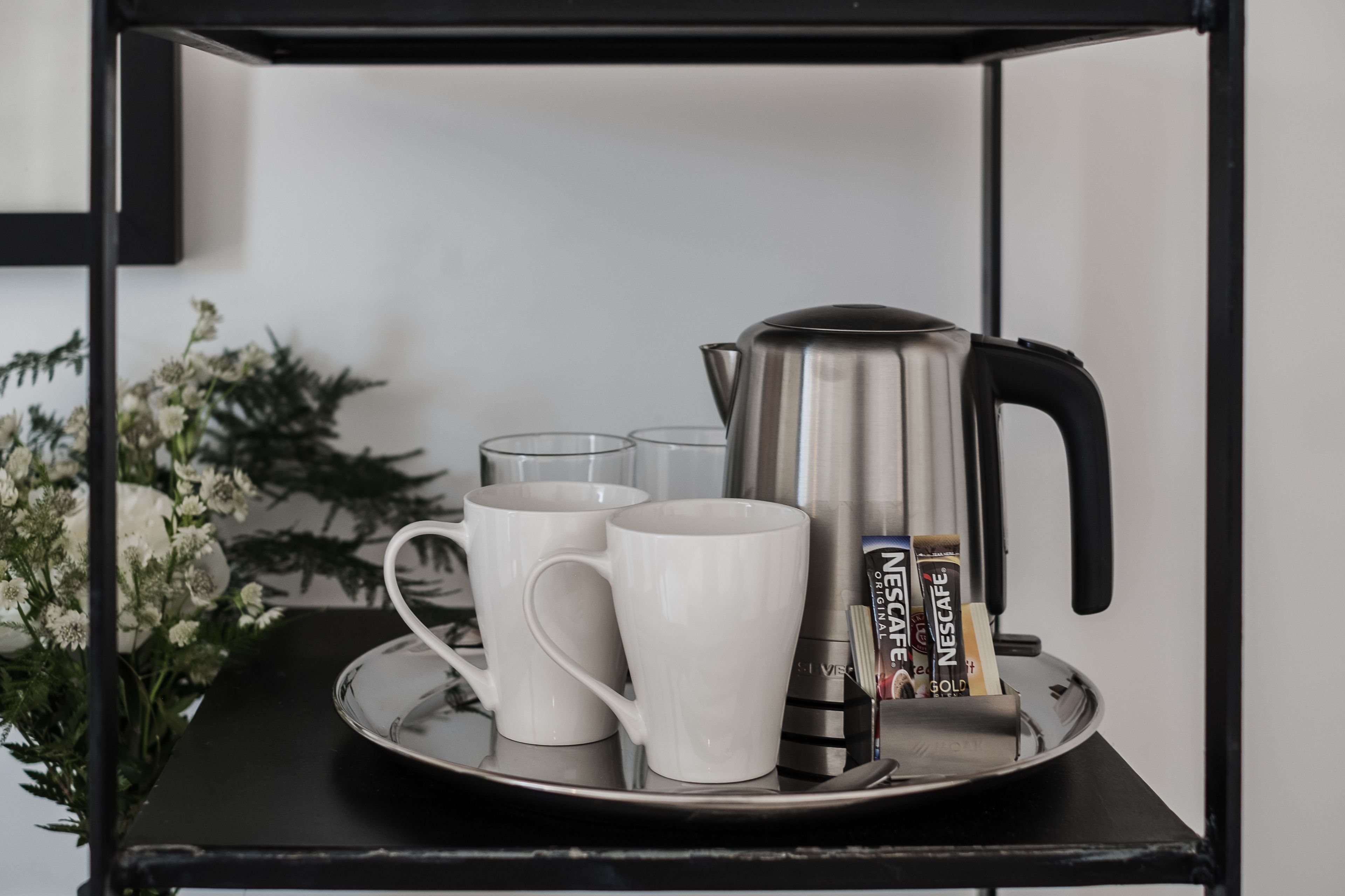 Un vassoio con una macchina da caffè, due tazze e due bicchieri su una mensola nera.