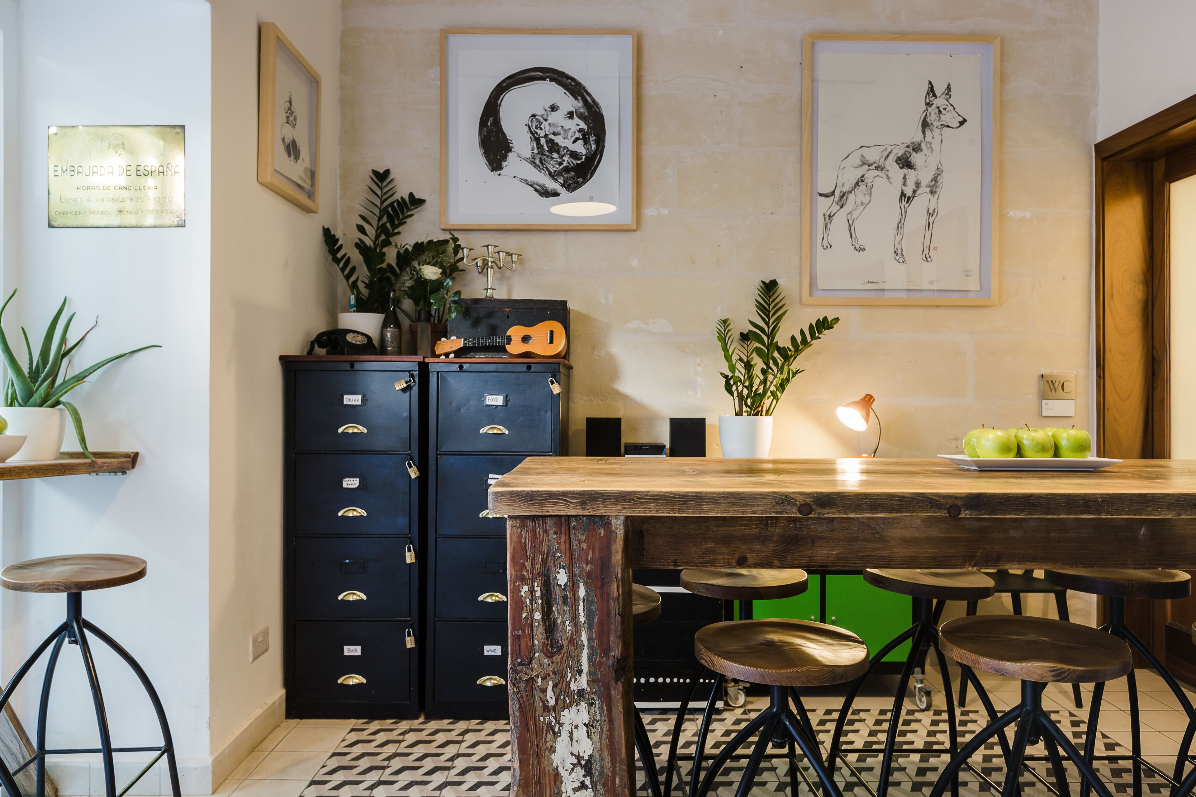 Una cocina con una isla de madera, taburetes de bar, un armario negro y obras de arte enmarcadas en la pared.