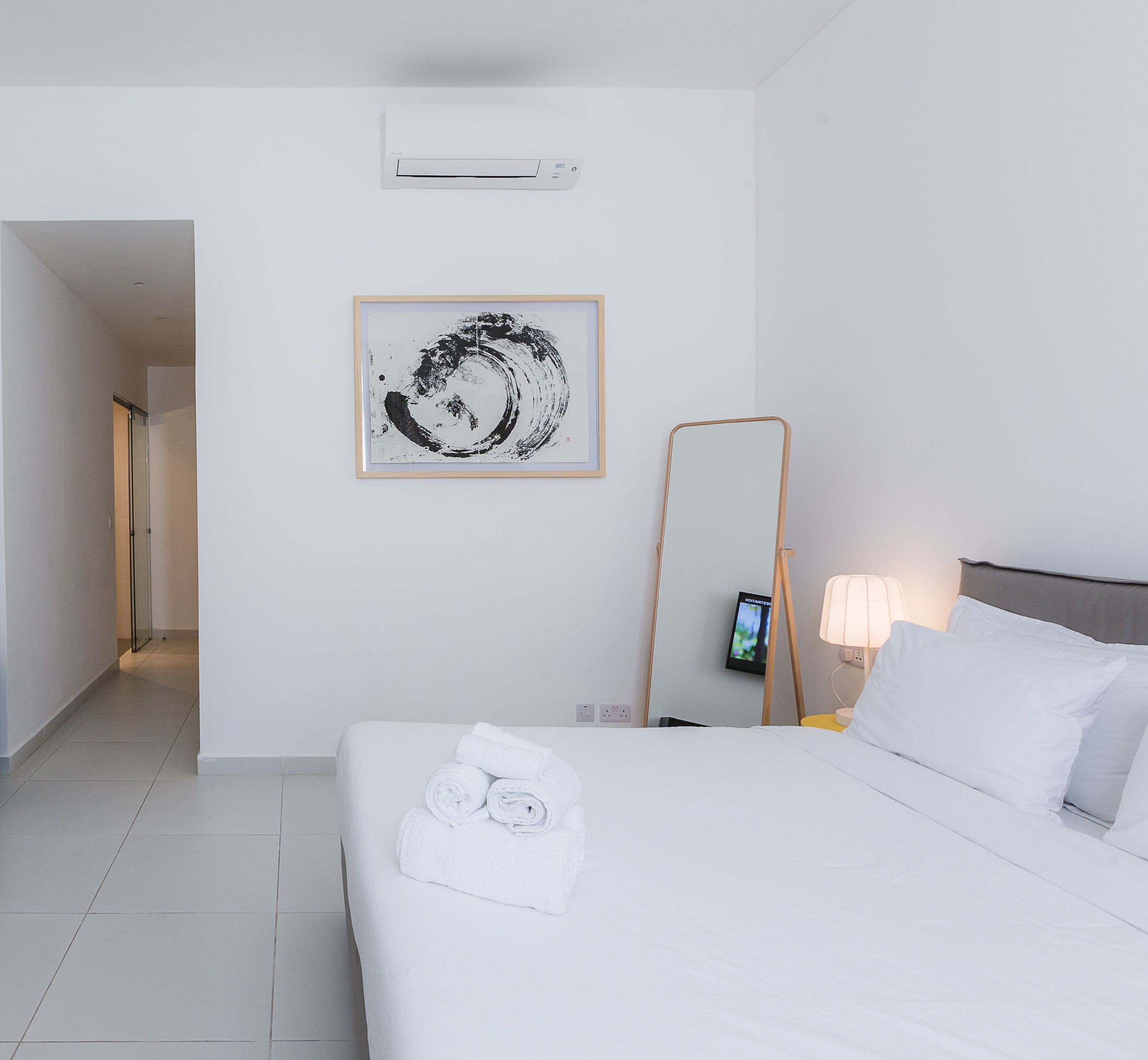 A hotel room with a bed, a bedside lamp, a mirror, and a framed artwork on the wall.