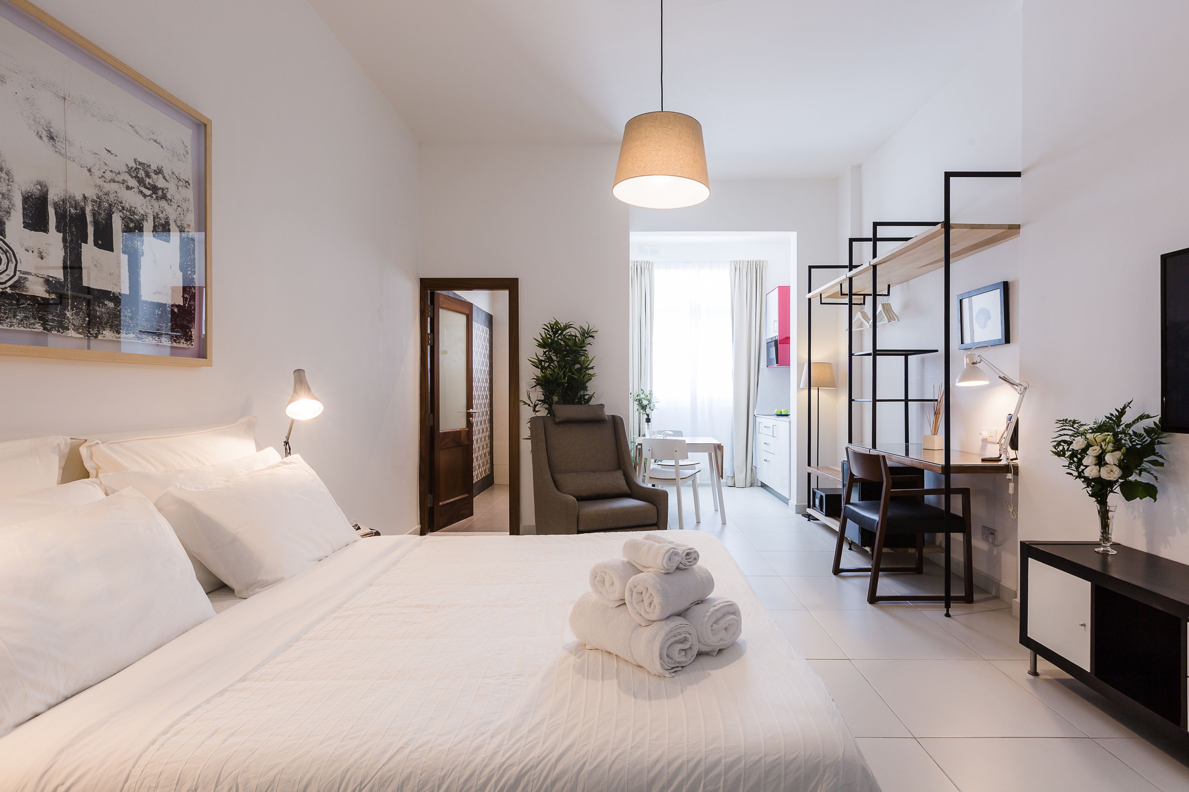 Una habitación de hotel con una cama bien hecha, un escritorio con una silla, un televisor y una zona de comedor con mesa y sillas.