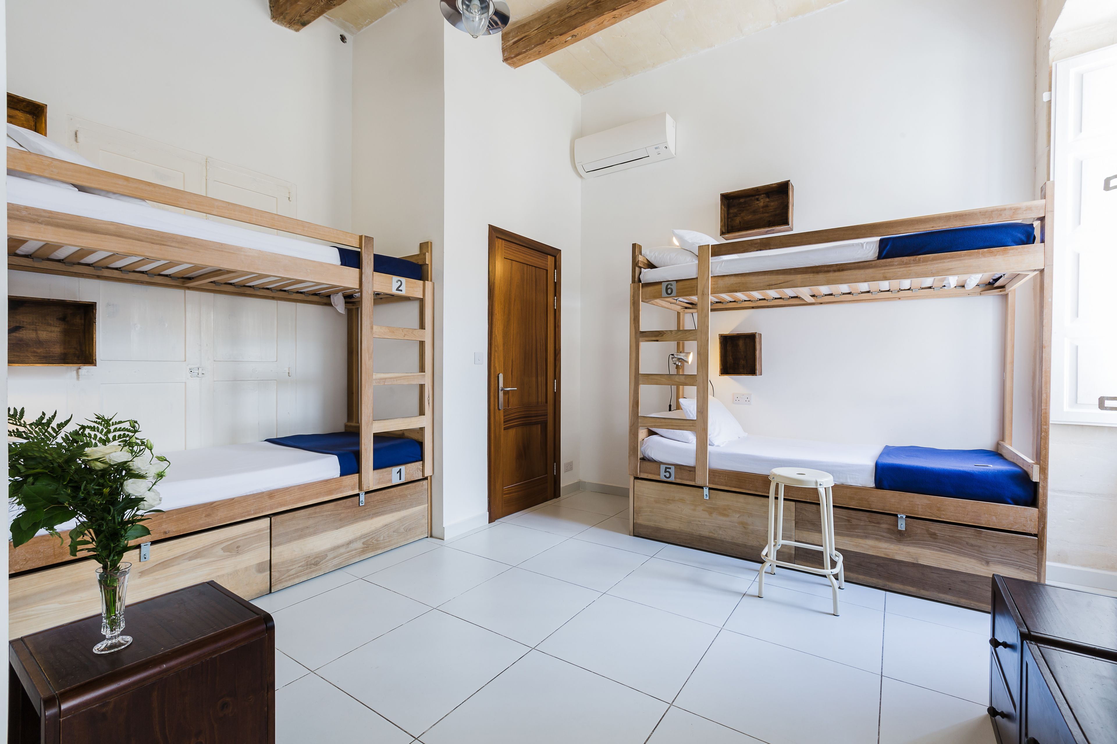 Ein Schlafsaalzimmer mit Etagenbetten, einem Holztisch, einem kleinen Hocker und einem Blumentopf.