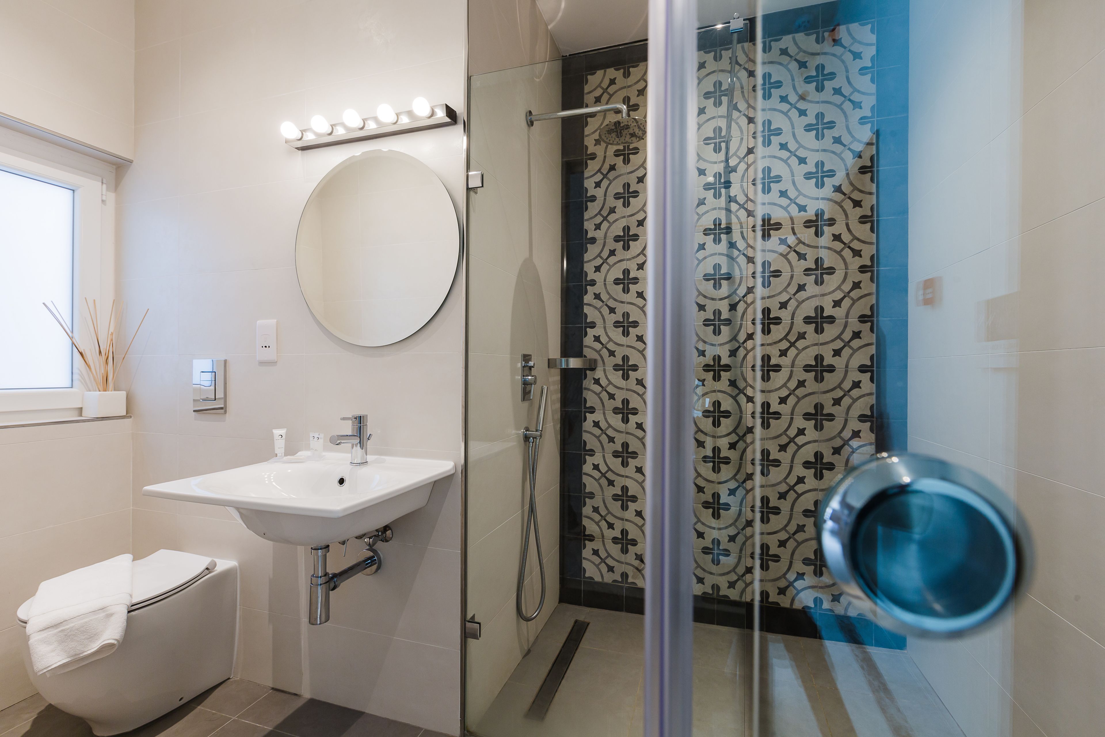 Un baño moderno con un lavabo blanco, un espejo redondo y una ducha con mampara de vidrio.