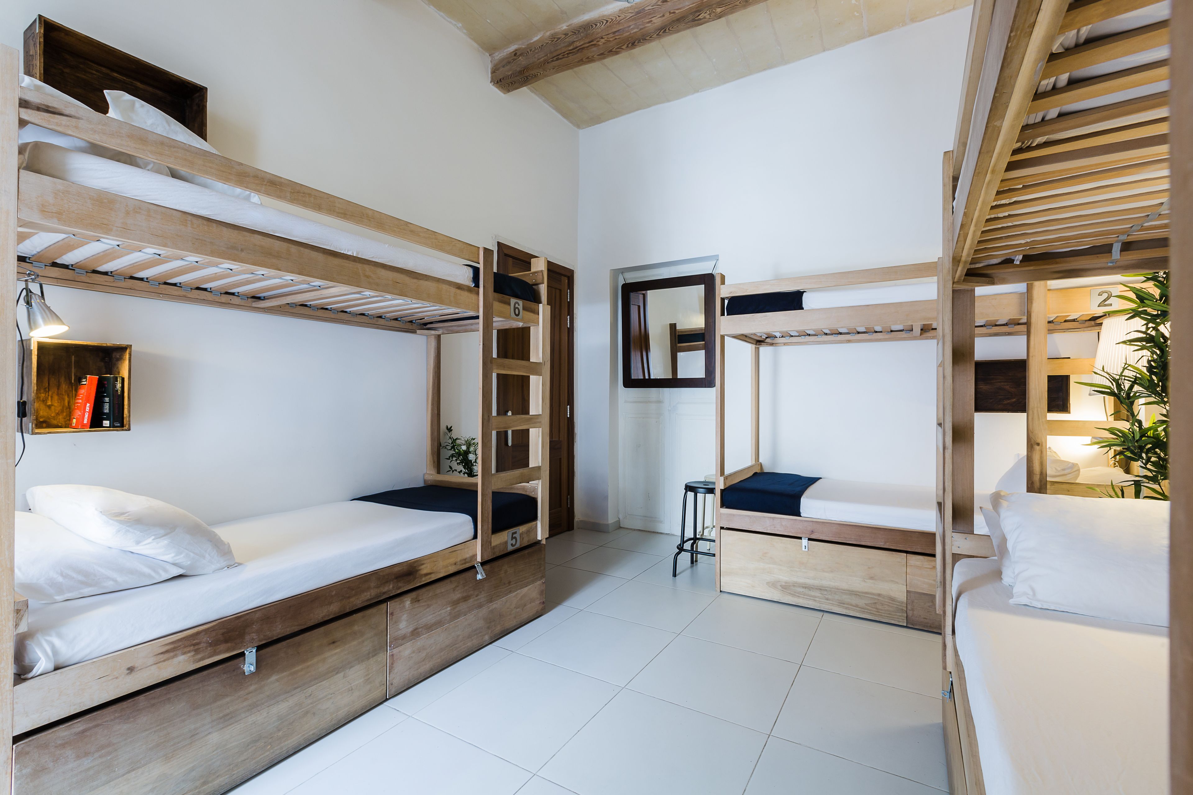 Ein Schlafsaalzimmer mit Etagenbetten, einem Spiegel, einem kleinen Hocker und einem Regal mit Büchern.