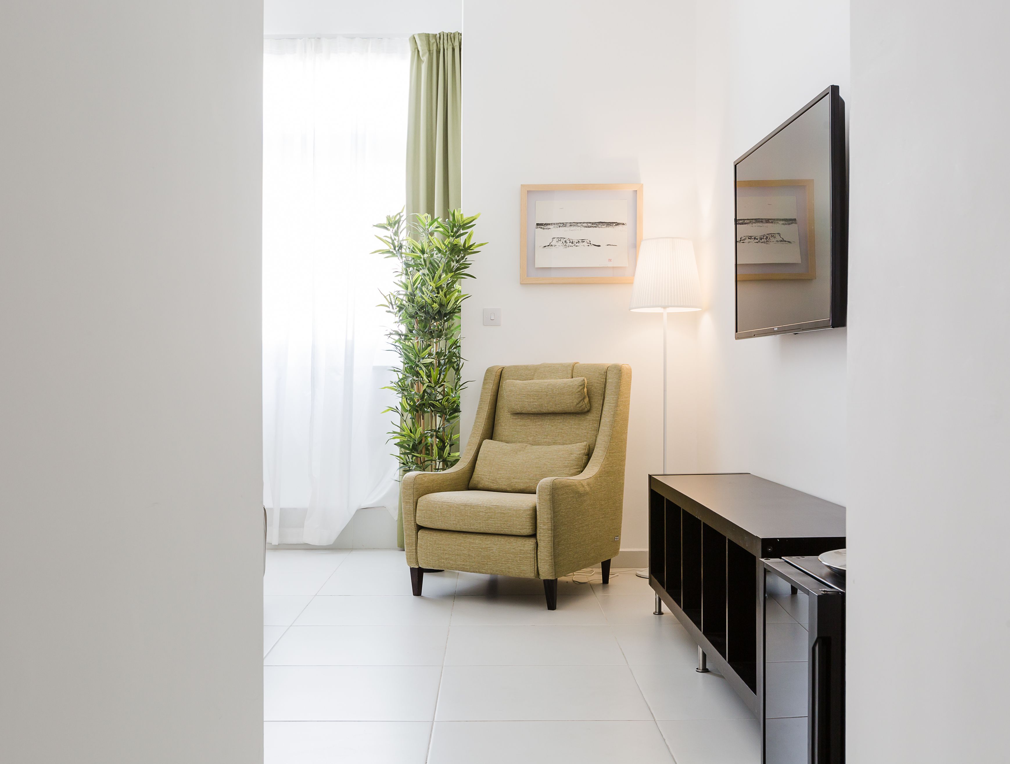 Ein modernes Wohnzimmer mit einem beigefarbenen Sessel, einer Stehlampe und einem großen Fenster mit leichtem Vorhang.