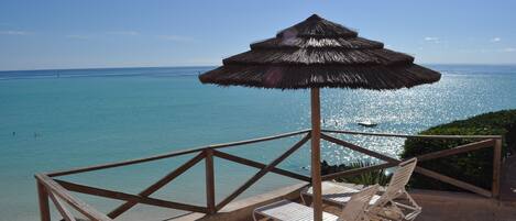Un espai relaxant a la vora de la platja amb una ombra de palla, seients ganduls blancs i vista a l'oceà.