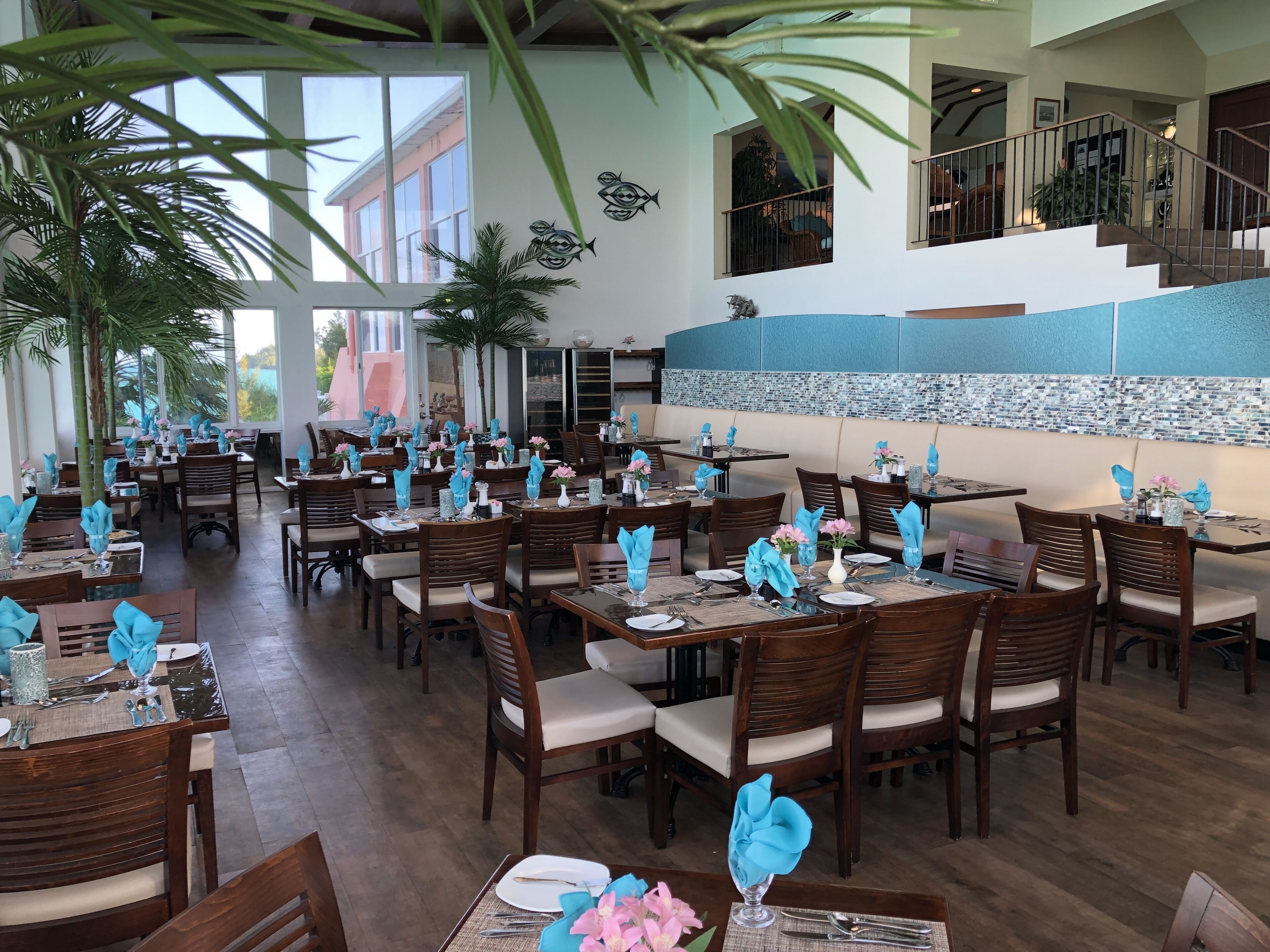 A restaurant with multiple dining tables, each set with blue napkins, white plates, and silverware.