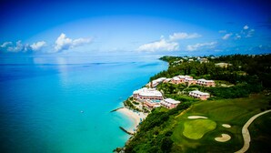 An aerial view of a coastal resort with a golf course, beachfront, and multiple buildings. - Pompano Beach Club (Southampton Parish)