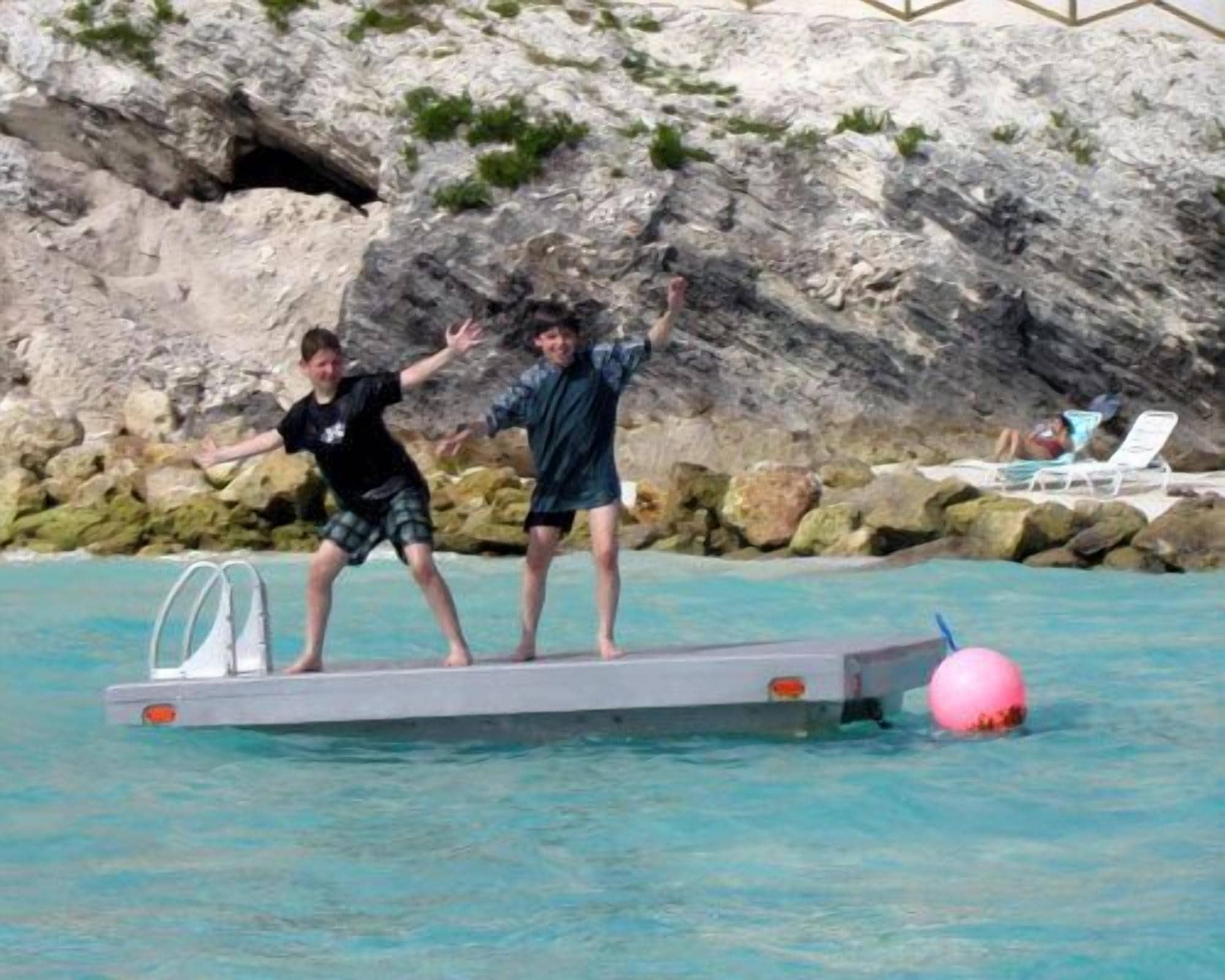 Zona de piscina amb una plataforma flotant i una persona dempeus a sobre.