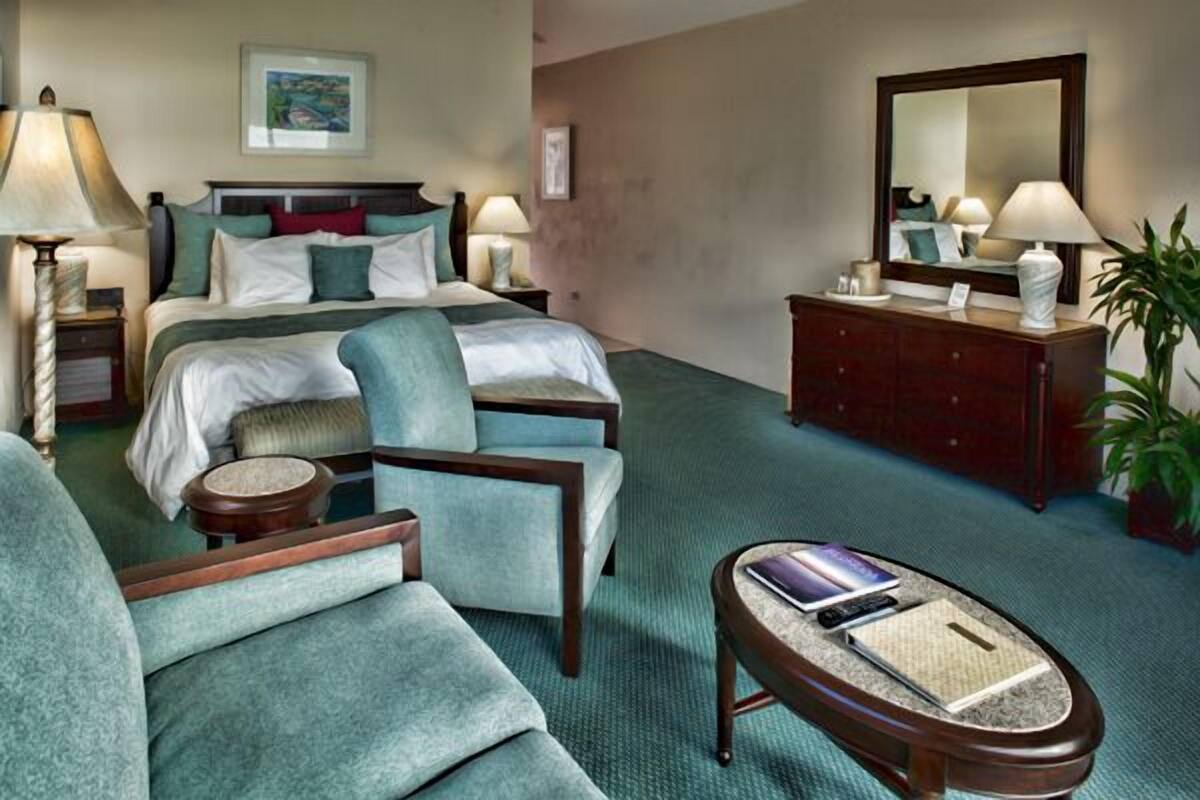 A hotel room with a bed, two armchairs, a desk, a dresser, and a mirror.