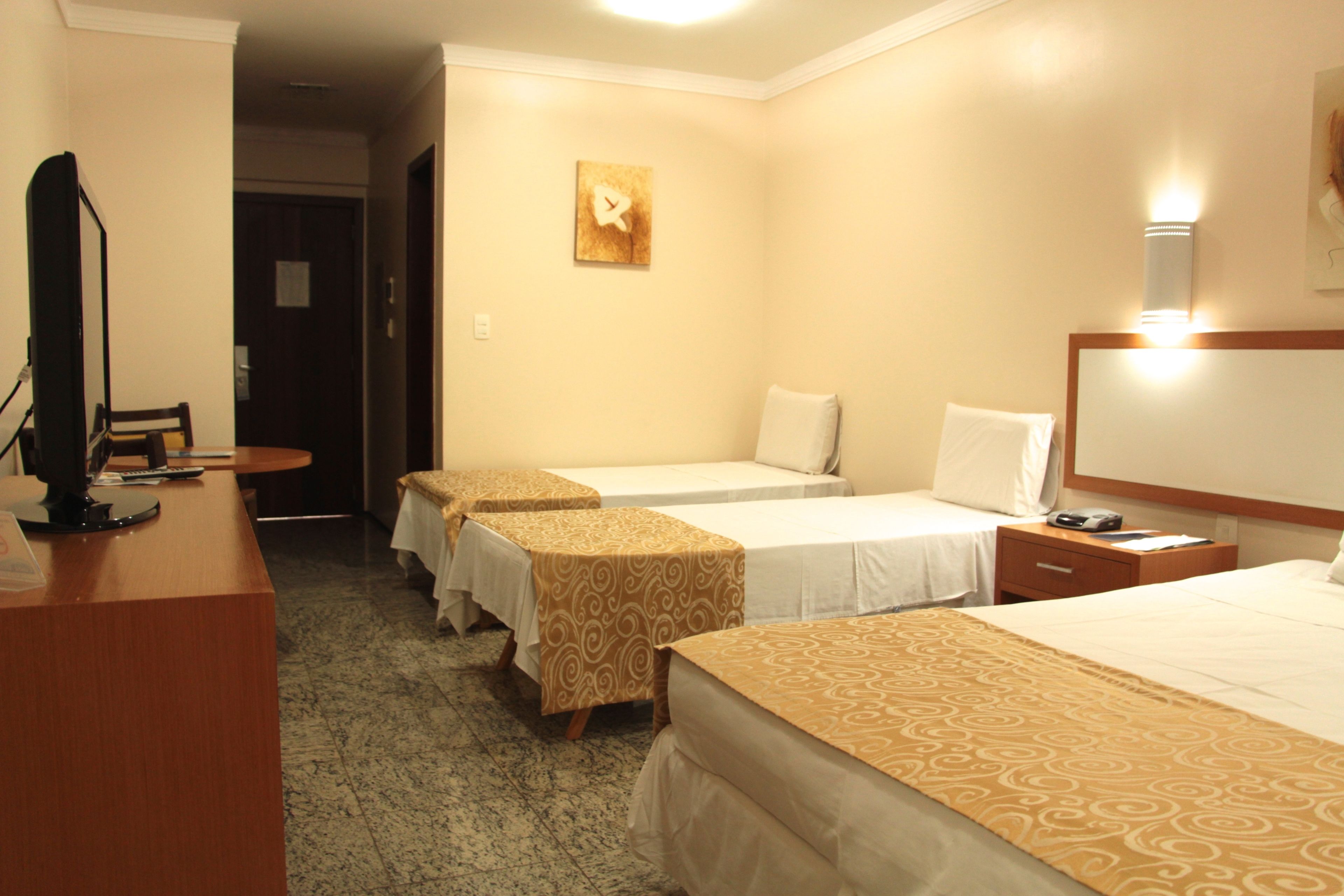 A hotel room with three single beds, a desk with a computer, and a small table.