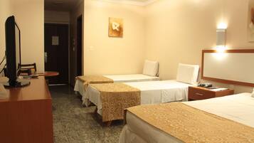A hotel room with three single beds, a desk with a computer, and a small table.