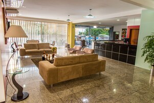 Um hall moderno com um sofá, cadeiras, uma mesa de centro de vidro e um balcão de recepção.