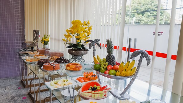 Una mesa de buffet con frutas, pasteles y una planta decorativa.