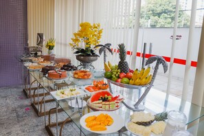 Una mesa de buffet con frutas, pasteles y una planta decorativa.