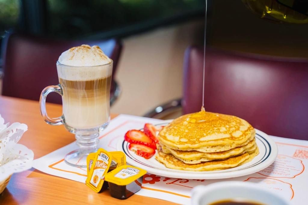 Un desayuno con una taza de café, una pila de tortitas y salsas sobre una mesa.