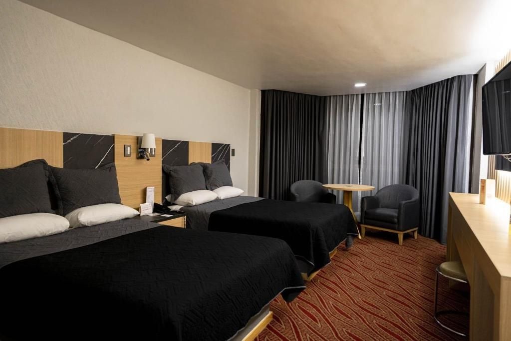 A hotel room with two beds, a desk, a chair, and a TV.