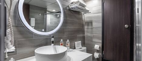 Une salle de bain moderne avec un miroir rond, un lavabo blanc et une porte en bois foncé.