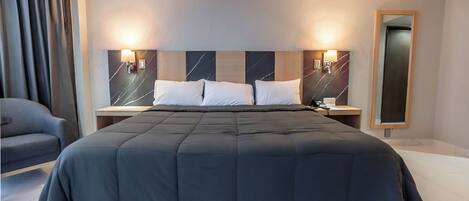 A modern hotel room with a large bed, two bedside tables, a chair, and a mirror.