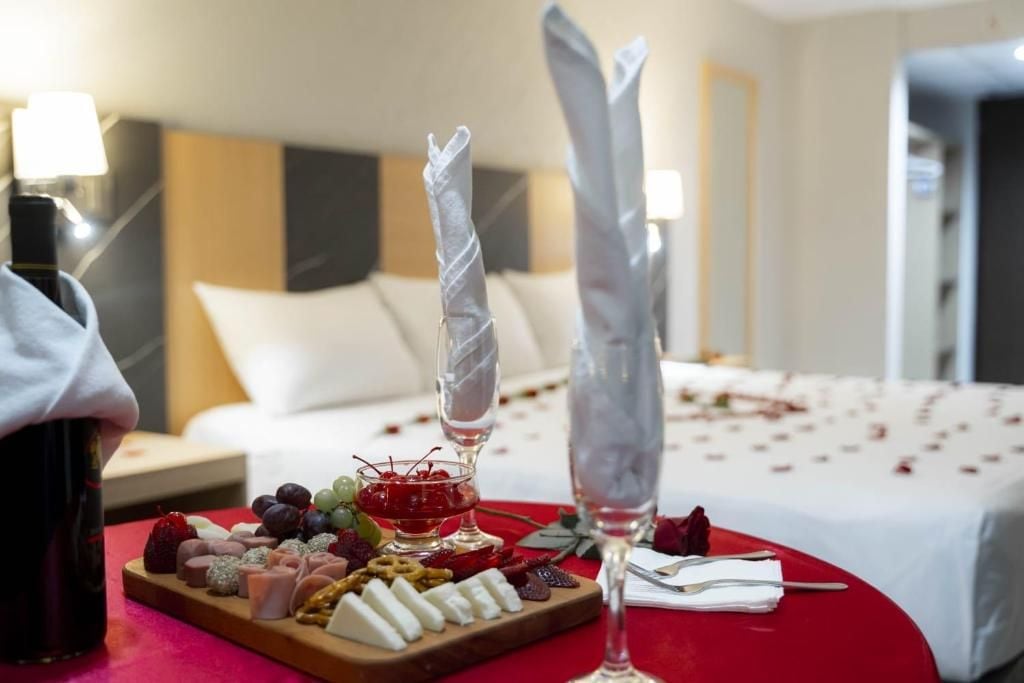 Quarto de hotel com uma mesa de café da manhã bem organizada, exibindo diversos queijos, frutas e uma garrafa de vinho.