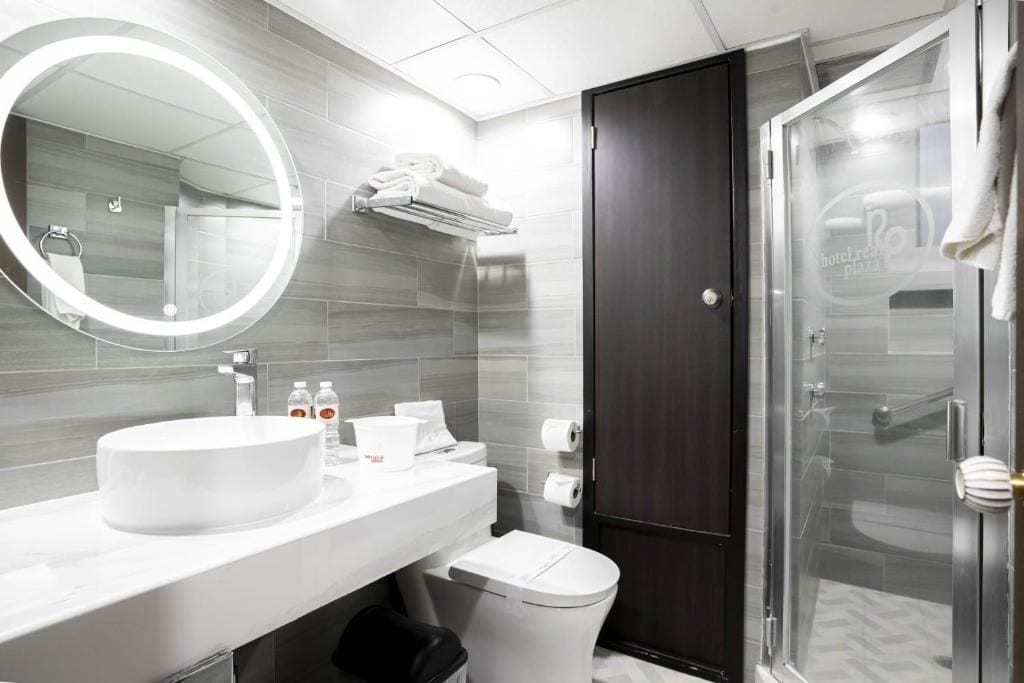 A modern bathroom with a round mirror, white sink, and a glass shower enclosure.