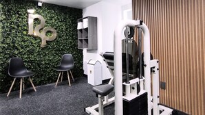 Un gimnasio moderno con equipo de ejercicio, dos sillas negras y una pared verde con un logotipo 'P'.