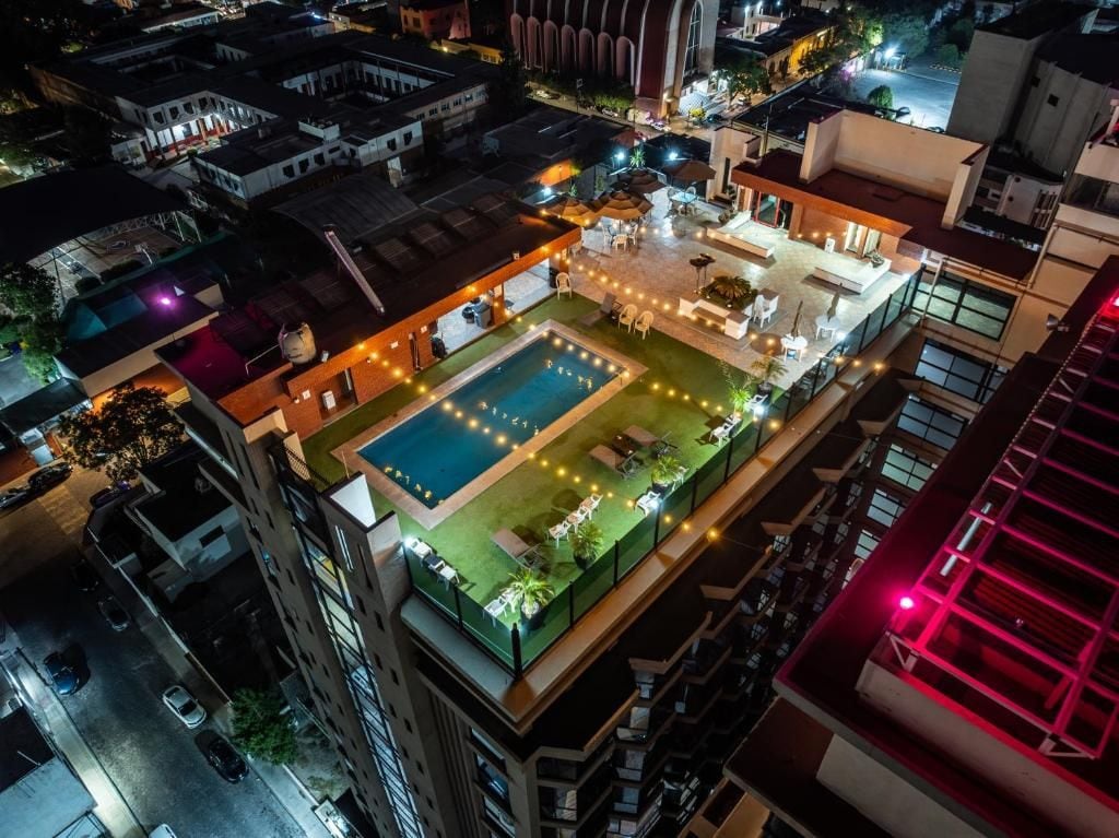 Un área de piscina en la azotea con múltiples sillones de descanso y sombrillas, rodeada de edificios.