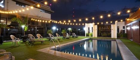 Zona de piscina exterior con sillas de descanso e iluminación con luces.