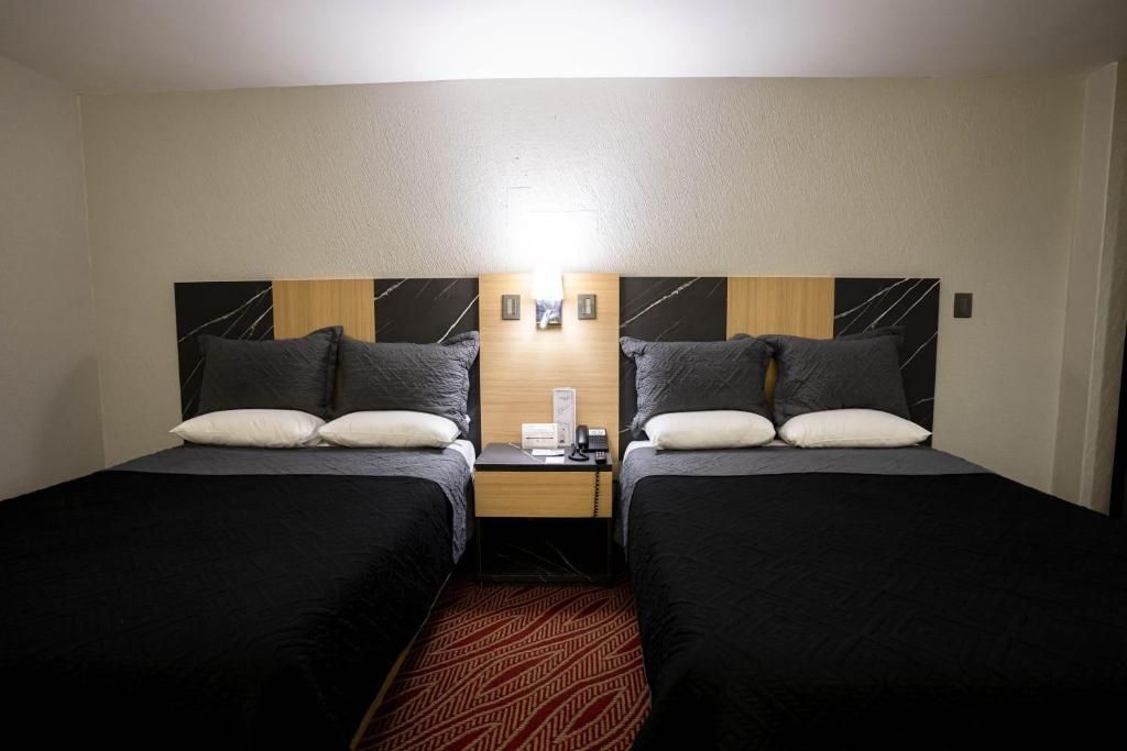 Et hotelværelse med to senge, et sengebord, en telefon og en lampe på væggen.