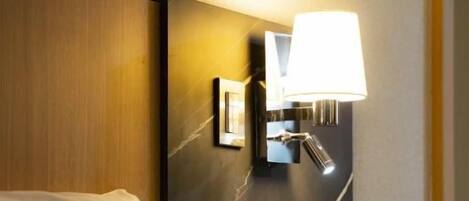 Una habitación de hotel con cama, lámpara de noche, teléfono y una lámpara de pared.