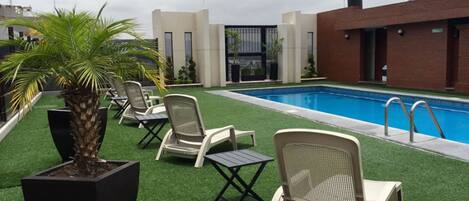 A rooftop pool area with artificial grass, lounge chairs, and a palm tree.