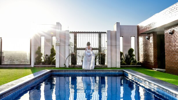 Una mujer con un vestido blanco de pie junto a una piscina con vistas a un paisaje urbano.
