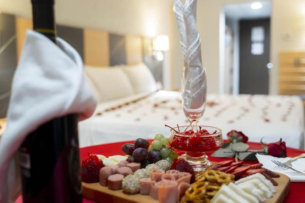 Une chambre d’hôtel avec un lit, une table de chevet sur laquelle se trouve une bouteille, et un plateau contenant divers en-cas et un verre d’un liquide rouge.
