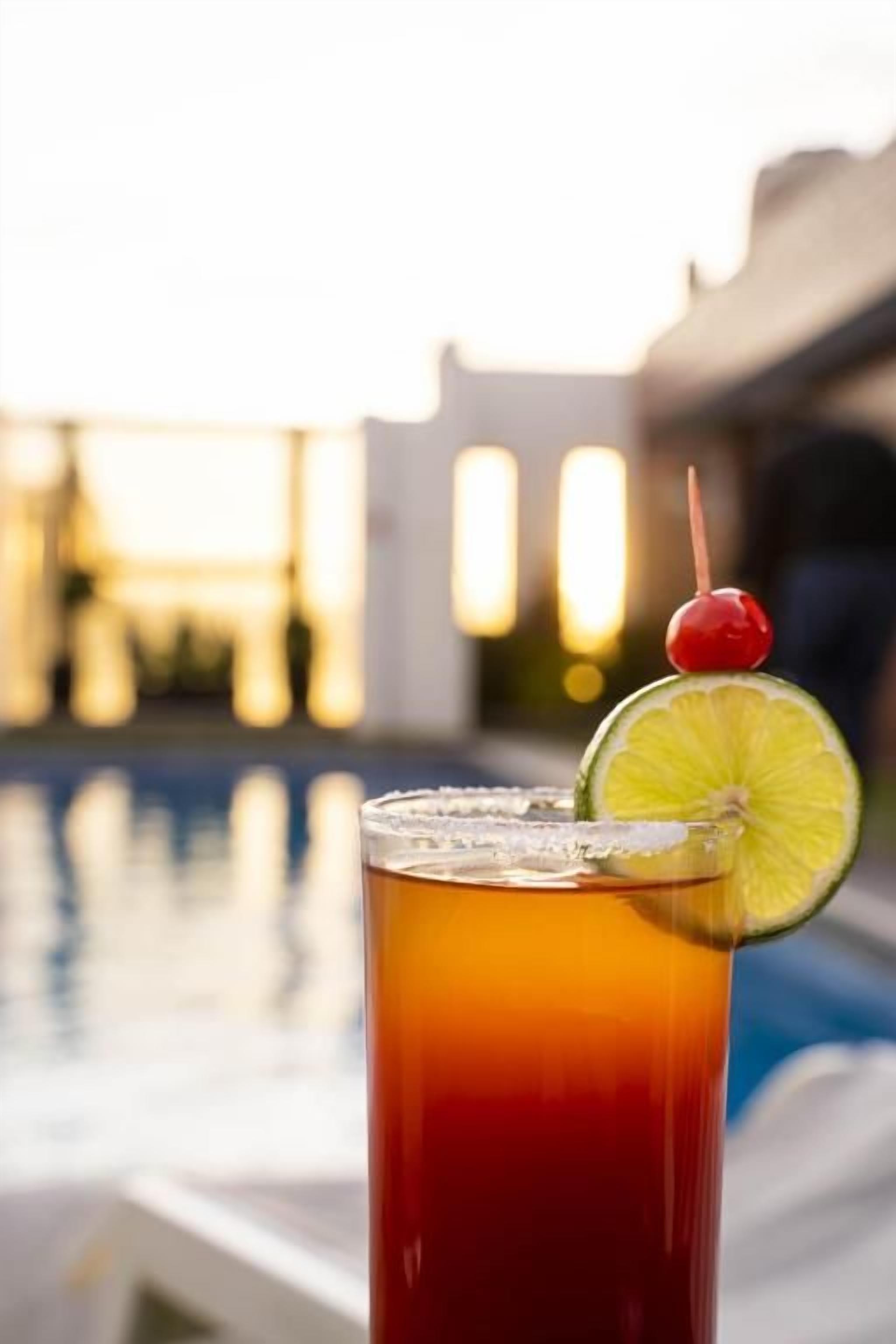 A glass of iced tea with a cherry and lime garnish, placed near a poolside area.