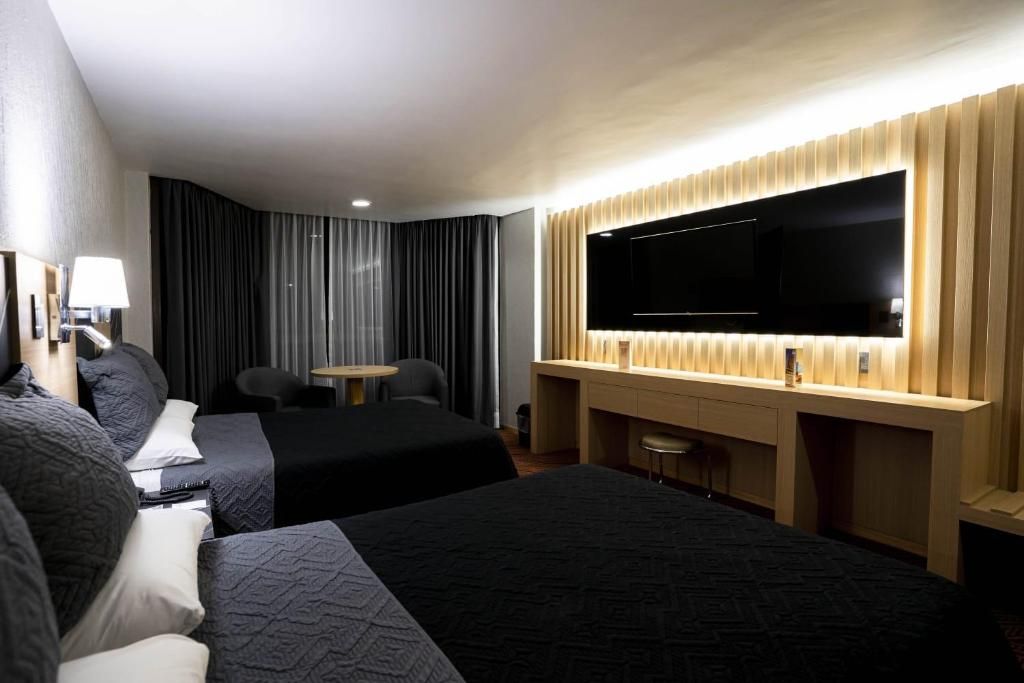 Habitación de hotel con dos camas, un escritorio, una silla, un televisor de pantalla plana y un ventanal con cortinas.